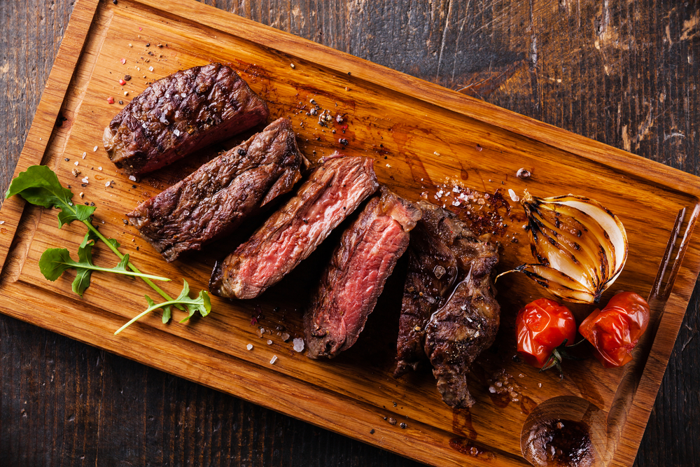 Sliced steak Ribeye with grilled onions and cherry tomatoes on cutting board on wooden background