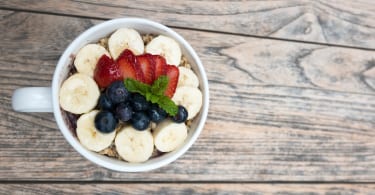 Acai bowl with strawberry, blueberry, banana, granola on wooden table.