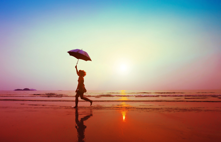 happy woman jumping with umbrella on the beach