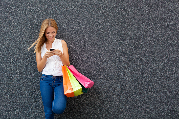 Happy young woman typing a message the phone after shopping