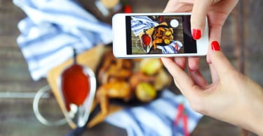 Woman taking photo of hot meat dishes on wooden background