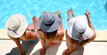 three beautiful young woman with sun hat sitting by the poolside of resort swimming pool during summer holiday